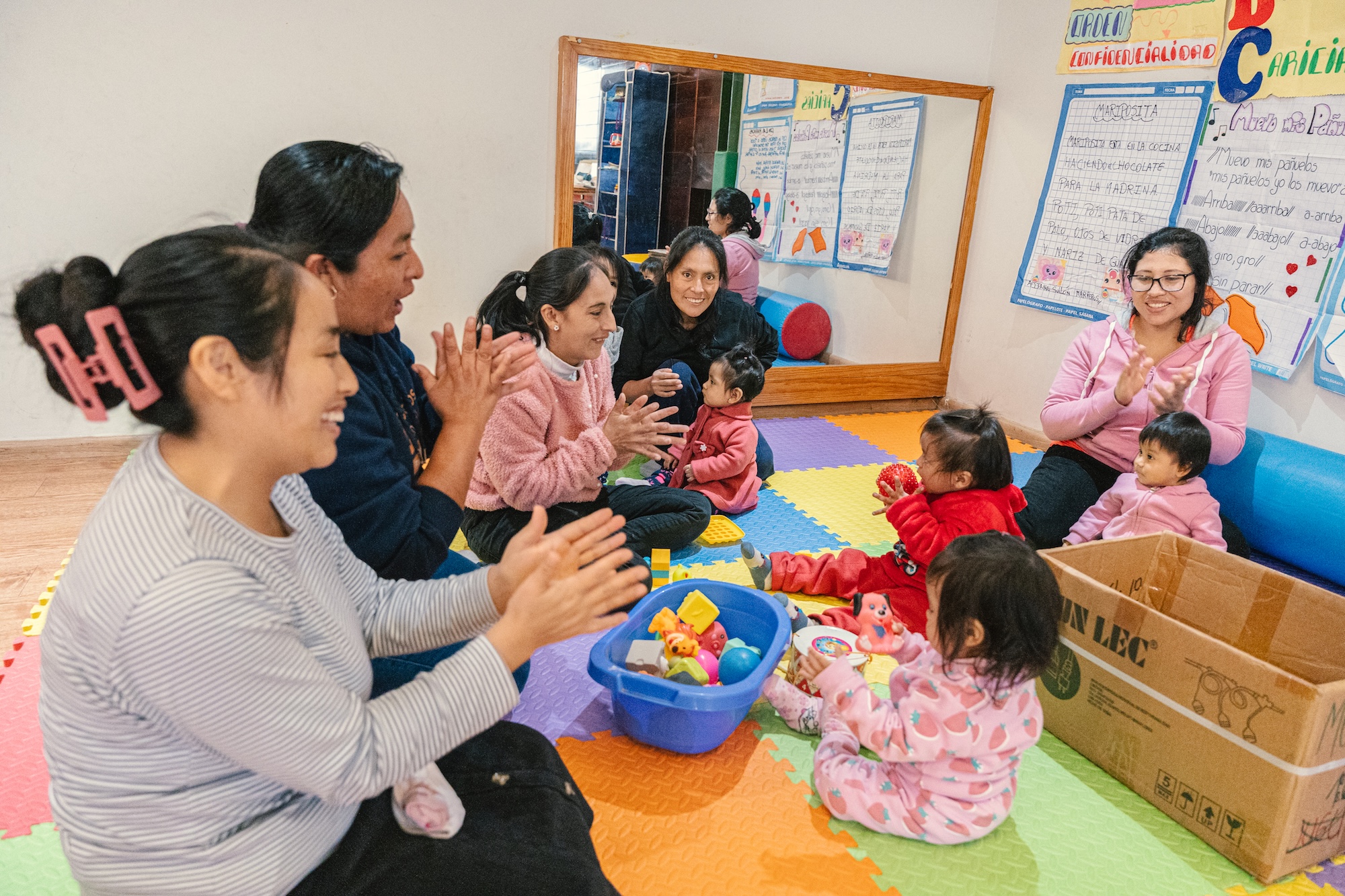 5 adults sit with 3 children in a childcare setting.